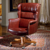 Brown leather presidential armchair with a high, wing-shaped back and buttoned upholstery, mounted on a swivel base with brass casters.