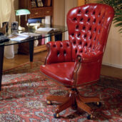 Red leather presidential armchair with a high, wing-shaped back and buttoned upholstery, mounted on a swivel base with brass casters.