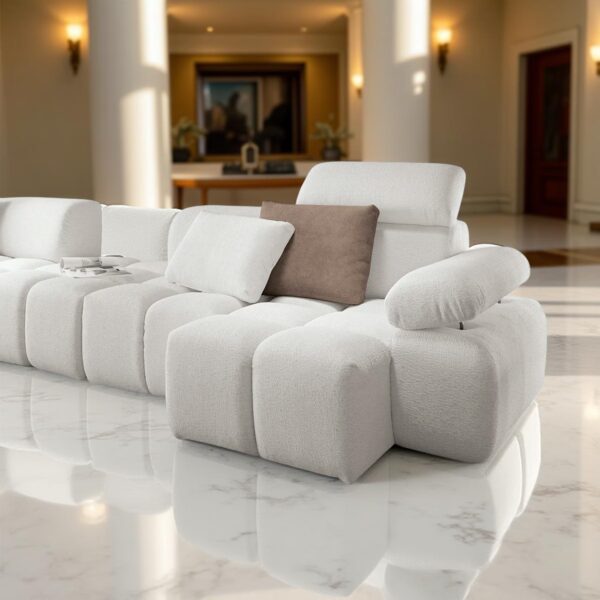 A modern white corner sofa with white and brown cushions, placed in a luxurious living room with marble flooring, wall lights, and elegant decorations.