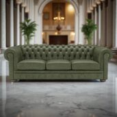 Divano Chesterfield in pelle verde posizionato in un salone lussuoso con pavimento in marmo, colonne alte, piante ornamentali e un arco che conduce a una stanza con lampadari