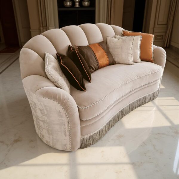 A classic beige sofa with a curved backrest, fringes at the base, and decorative cushions in various shades, set in an elegant room with marble flooring and columns.