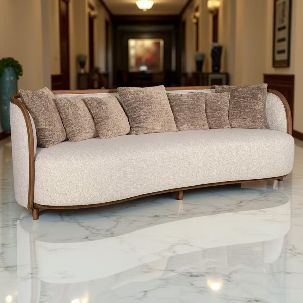 Divano moderno curvo in tessuto beige con struttura in legno e sette cuscini marrone-beige, posizionato in un corridoio elegante con pavimento in marmo, pannelli in legno e decorazioni artistiche