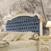 Elegant Italian luxury bed with blue tufted headboard and ornate details in a sophisticated bedroom setting.