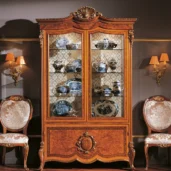 Luxury Italian cabinet with fine china, elegant chairs, and ornate design in a sophisticated setting.