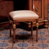 Elegant wooden stool with ornate legs, upholstered in patterned fabric, on intricate tiled floor. Handcrafted luxury furniture.