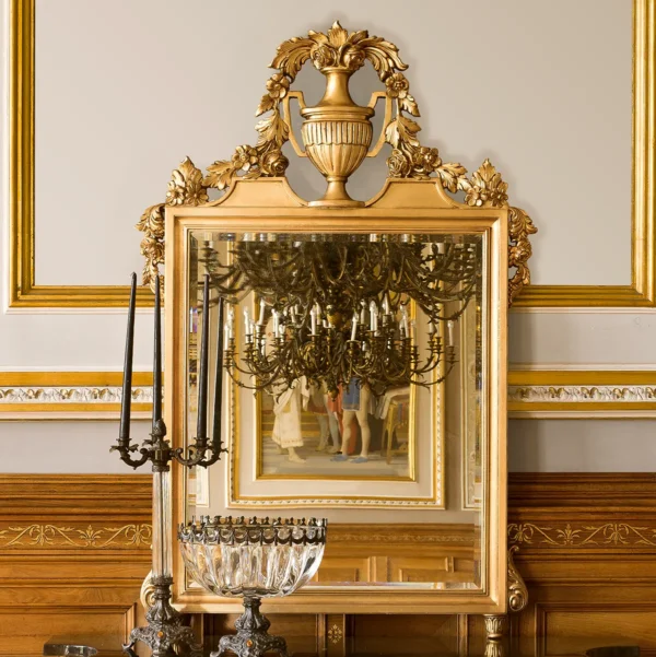 Ornate gold mirror with intricate detailing reflects elegant chandelier in classic villa interior. Handcrafted luxury design.