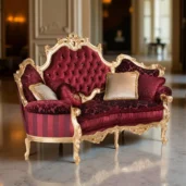 Ein luxuriöses Sofa mit goldenem Gestell und rotem, gestepptem Bezug, verziert mit goldenen und roten Kissen, platziert in einem eleganten Raum mit Marmorboden, Säulen und Wandleuchten.