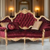A luxurious sofa with a golden frame and tufted red upholstery, adorned with gold and red cushions, set in an elegant room with marble flooring, columns, and wall sconces.