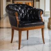 Black leather armchair with tufted back, brass nailhead trim, and wooden legs on marble floor