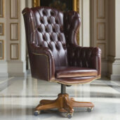 Poltrona direzionale in pelle bordeaux con schienale trapuntato, borchie in ottone e base in legno con ruote