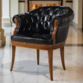 Black leather armchair with a curved back and buttoned Chesterfield capitonné upholstery, resting on a wooden base with wooden legs.