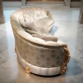 Divano curvo di lusso con dettagli dorati, tessuto chiaro decorato e cuscini eleganti in un atrio con colonne e pavimento in marmo.