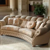 Divano curvo beige di lusso con dettagli ornamentali e cuscini floreali, ambientato in un interno classico ed elegante.