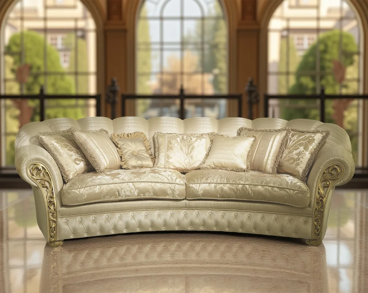 Divano di lusso color crema con dettagli dorati, stile classico, ambientato in un salone elegante con grandi finestre ad arco.