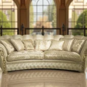 Divano di lusso color crema con dettagli dorati, stile classico, ambientato in un salone elegante con grandi finestre ad arco.