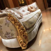 Divano curvo di lusso con dettagli dorati, tessuto chiaro decorato e cuscini eleganti in un atrio con colonne e pavimento in marmo.