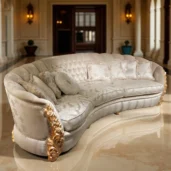 Divano curvo di lusso con dettagli dorati, tessuto chiaro decorato e cuscini eleganti in un atrio con colonne e pavimento in marmo.