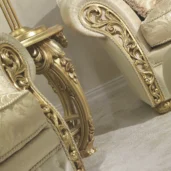 Divano angolare di lusso in velluto grigio chiaro con dettagli dorati e cuscini decorativi, ambientato in un elegante salone classico.