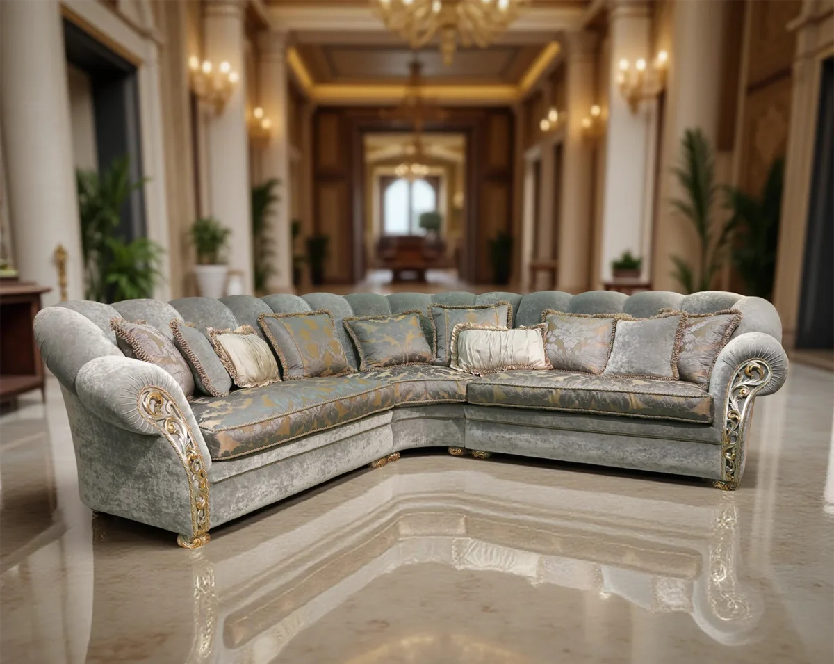 Luxury light grey velvet L-shaped sectional sofa with gold accents and decorative cushions, set in an opulent classical interior.