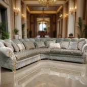 Luxury light grey velvet L-shaped sectional sofa with gold accents and decorative cushions, set in an opulent classical interior.