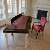 Dark-wood executive desk with curved top and burgundy leather inlay, fluted gold-finish legs; luxury furniture for the home office.