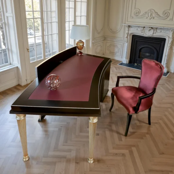 Scrivania direzionale in legno scuro con top curvo e inserto in pelle bordeaux, gambe scanalate finitura oro; arredo di lusso per studio.