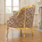 Louis XV style classic armchair featuring a carved wood and gold leaf finish frame, upholstered in beige damask fabric with decorative cushions, on a white background.