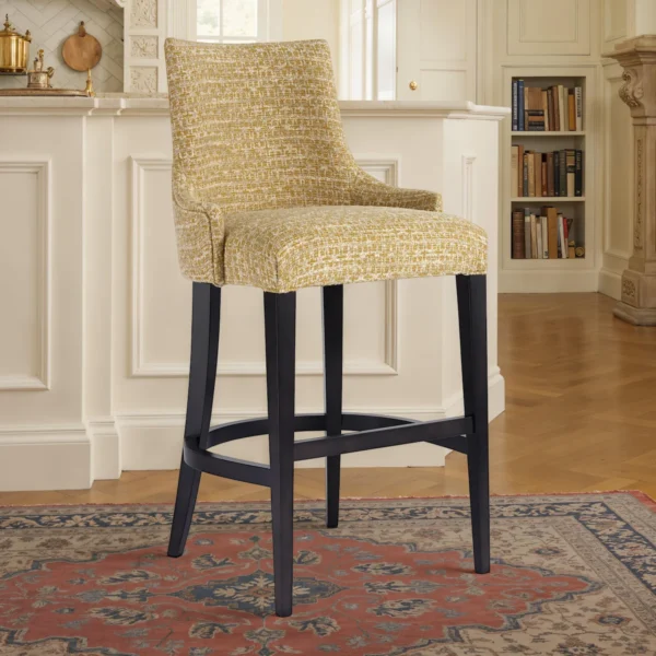 Counter‑height upholstered barstool with wraparound back, mustard textured fabric, dark wood legs and curved footrest stretcher – Marzorati.