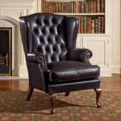 Poltrona wingback in pelle nera, schienale capitonné, braccioli arrotolati, bordatura con borchie e gambe in legno a cabriole.