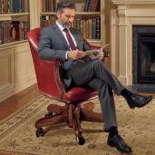 Luxurious red leather executive swivel armchair with classic design, placed in a refined study with bookshelves full of books, fireplace, and oriental rug, perfect for high-end executive furniture and professional comfort.