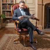Luxurious burgundy leather executive swivel armchair with classic design, placed in a refined study with bookshelves, fireplace, rug, and plant, perfect for high-end executive furniture and elegant comfort.