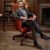 Poltrona direzionale girevole in pelle marrone cognac di lusso con design classico, posizionata in uno studio raffinato con librerie, scrivania e camino, ideale per arredi executive di alta gamma e comfort caldo e professionale.