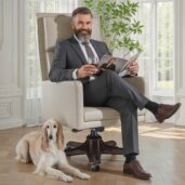Smiling man in suit seated in a luxurious cream leather executive swivel armchair, reading a magazine with a glass in hand in a bright lounge with windows and plant, perfect for high-end home office furniture and relaxed comfort.