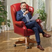 Elegante poltrona executive in pelle rossa con schienale alto, base girevole in legno e ruote, ideale per arredi ufficio di lusso.