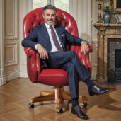 Luxurious vibrant red leather executive swivel armchair with classic design, placed in a refined lounge with fireplace, decorative vase, and painting, perfect for high-end executive furniture and energetic comfort.