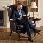 Poltrona da lettura in pelle marrone scuro con schienale alto capitonné, borchie decorative e gambe in legno