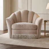 Luxury living room armchair with enveloping shell backrest, fringe skirt and soft neutral upholstery in fine Italian fabrics.