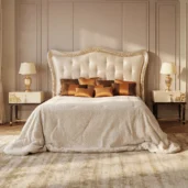 Luxury double bed with tall carved wood headboard, ivory tufted Italian upholstery and bronze decorative cushions in an elegant bedroom.