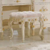 Eleonor pouf in hand-carved wood with plush upholstered cushion and ornate details.