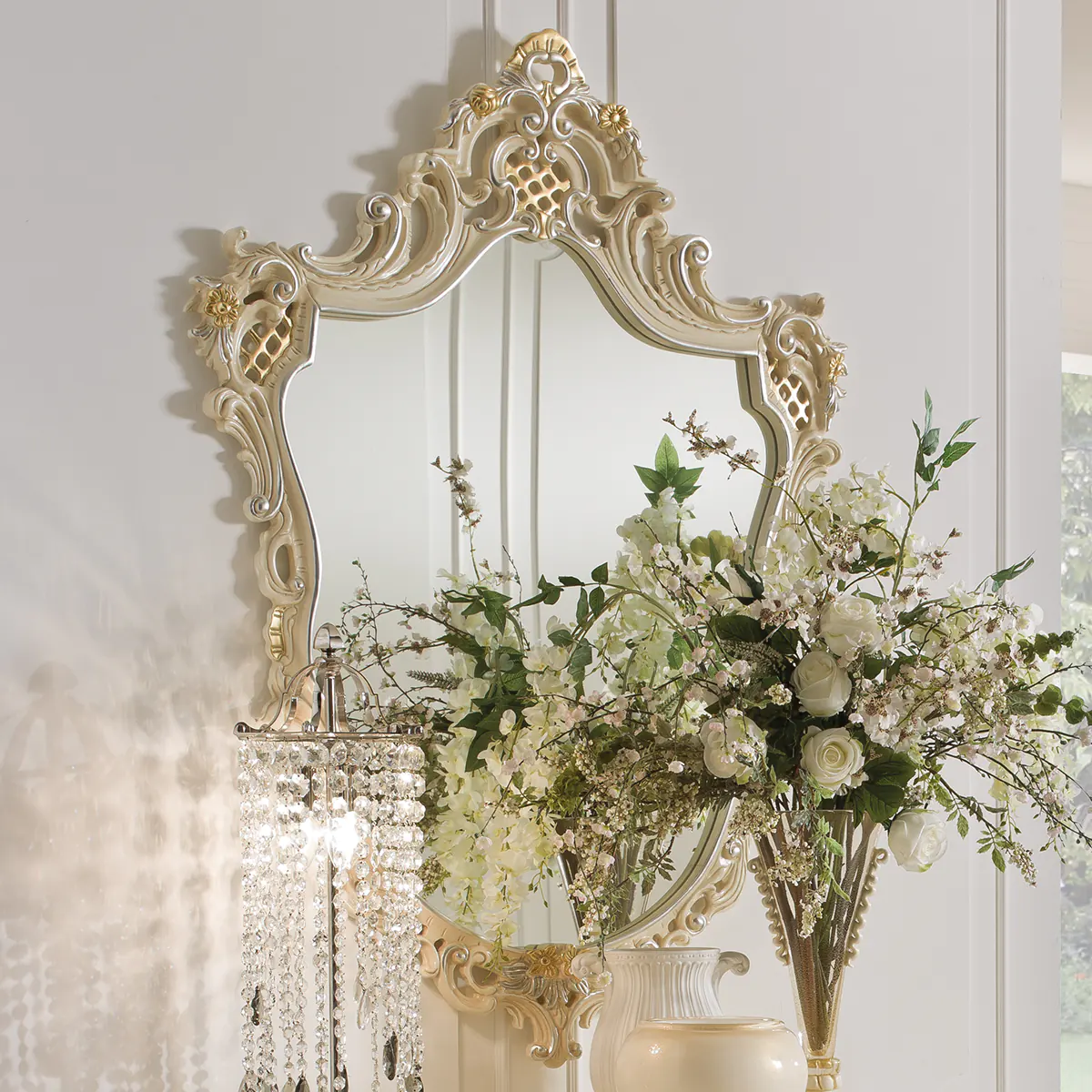 ELEONOR mirror EN Eleonor hand-carved wood mirror with ornate frame, styled with flowers and a crystal chandelier.