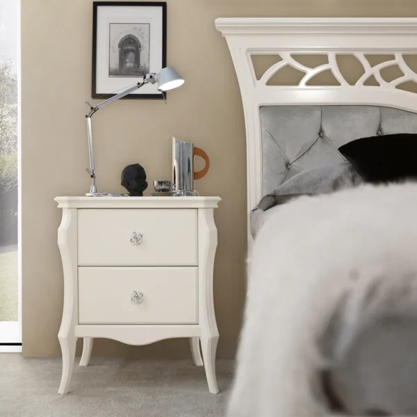 Monte Carlo nightstand in solid wood with ivory lacquer finish, next to upholstered bed.