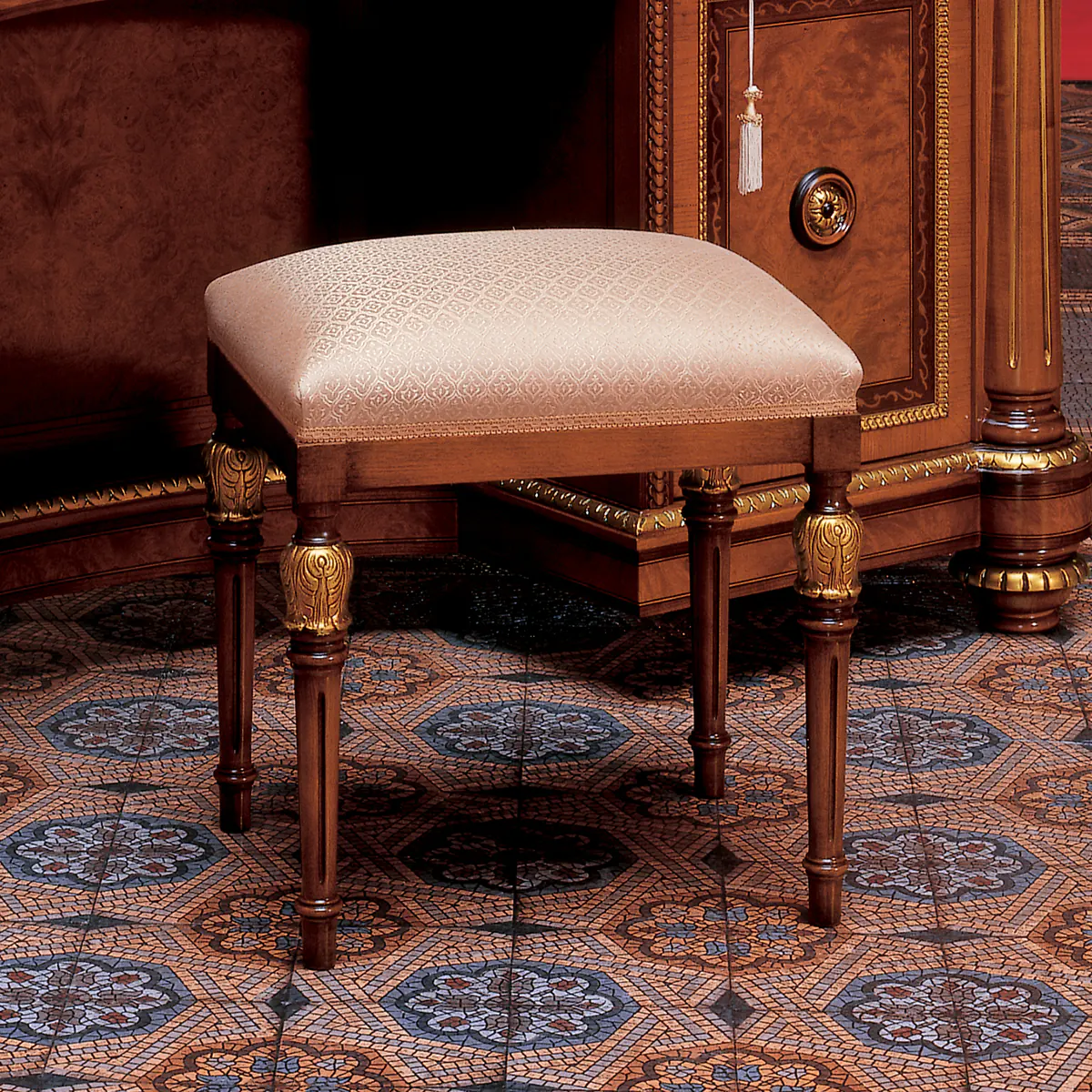 SENATOR stool Elegant Senator stool with ornate legs, upholstered in patterned fabric, on an intricate tiled floor.
