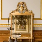 Ornate gold Senator mirror with intricate detailing reflecting an elegant chandelier in a classic villa interior.
