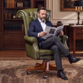 Classic green leather executive office chair with high tufted back, padded arms, wooden swivel base and casters